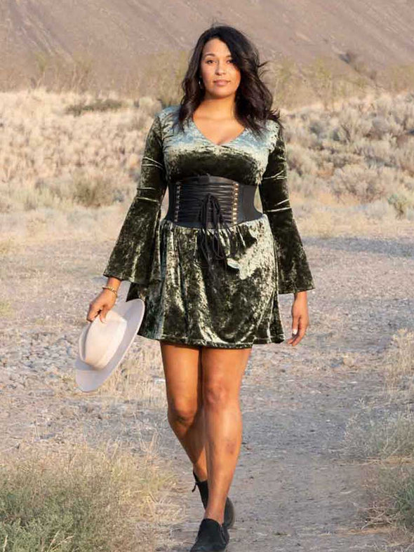 Woman wearing a muted green crushed velvet dress wearing a black wide lace up corset belt