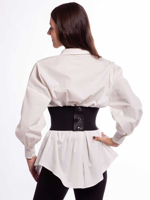 Woman wearing a white tunic and black leggings with a black laced corset on top back snap closure view