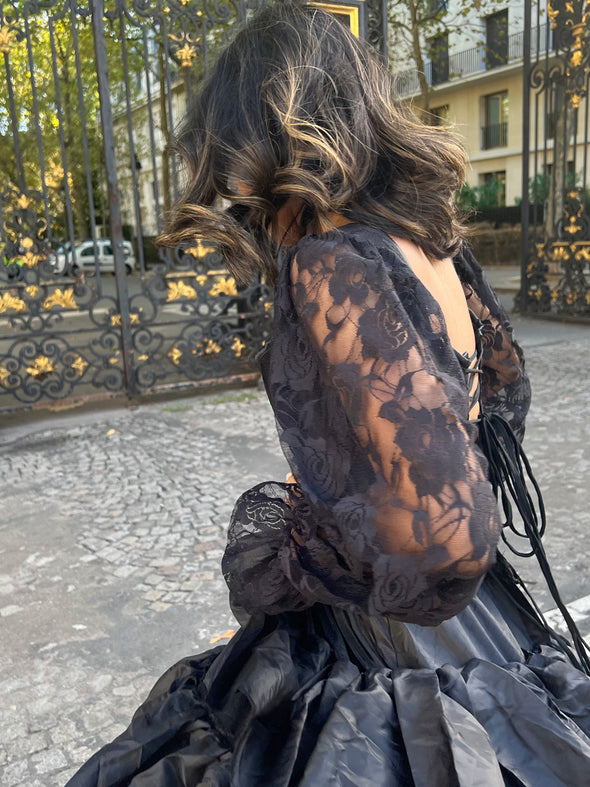 Detail of a long sleeved black lace corset styled top worn with a black skirt