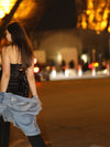 Model wearing a black chiffon and satin cropped fashion corset top with dark jeans and a washed jean jacket back walk away view